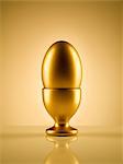 Golden egg in egg cup holder against gold background