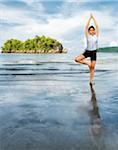 Thai girl doing a yoga position (tree pose) on Nopparat Thara Beach in Krabi Thailand.