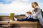 Baby girl wearing sun hat sitting on groyne with mother