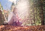 Mother and daughter sitting on autumn leaf covered forest floor