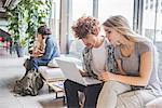 Co-workers working on laptop on sofa by window