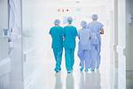 Rear view of four medical staff wearing scrubs walking in hospital corridor