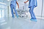Two medics urgently pushing hospital bed in corridor