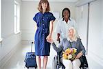 Daughter and hospital orderly pushing senior female patient in wheelchair