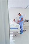 Male nurse using blood pressure gauge on senior female patient in hospital bed