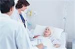 Doctors explaining to senior female patient in hospital bed