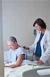 Female doctor listening to senior male patient back with stethoscope