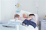 Senior female patient cuddling grandsons on hospital bed