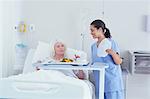 Nurse serving lunch to senior female patient in hospital bed