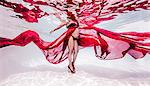 Underwater view of pregnant woman draped in sheer red fabric