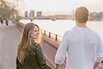 Rear view of couple strolling on waterfront at sunset, Battersea Park, London, UK