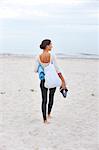 Young woman with exercise mat standing on beach