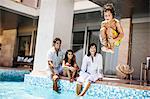 Young boy cannonballs into a pool while his smiling family watch.