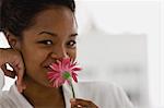 Portrait of a young woman smelling a pink daisy.