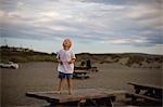 A young boy stands on a picnic table at the beach.