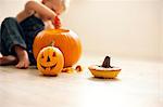 Young boy sitting on the floor uses a tool to hollow out a big pumpkin with a finished small Jack O'Lantern in front of him.