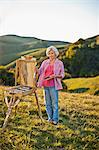 Mature woman painting on a scenic hillside.