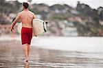 Man walking along the beach with his surfboard.