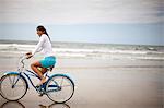 Young woman riding her bike on the beach.