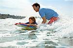 Father teaching young son how to ride a wave on a boogie board.