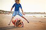 Brother and sister playing leapfrog at the beach.