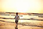 Preschool age boy running along the beach at sunset.