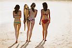 Rear view of three young women in bikinis with a surfboard