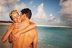 Smiling mid-adult woman being kissed on the cheek by her husband on a beach.