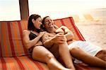 Happy mid-adult couple laughing while lying side by side on a deck chair at a beach resort.