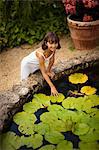 Portrait of a smiling young girl touching a lily pad in a lush garden fishpond.