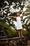 Smiling young girl having fun balancing on the stone wall of a garden fishpond.