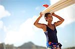 Mid adult woman carrying a surfboard on a beach.