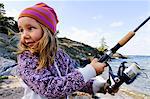 Girl holding fishing rod beside sea