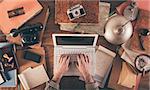 Messy vintage desktop with laptop and male hands typing, top view