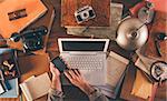 Messy vintage desktop with laptop and male hands using a smart phone, top view