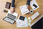 Businessman working at office desk and checking financial reports with computers and paperwork around, top view