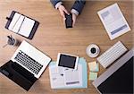 Businessman working at office desk hands top view with laptop and financial reports: he is using a mobile touch screen smart phone