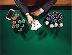 Elegant male poker player with smartphone holding two aces with stacks of chips all around, hands detail top view