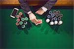 Elegant male poker player with smartphone looking at his cards with piles of chips all around