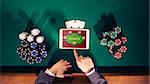 Poker player's hands with digital tablet, stacks of chips and cards on green table, top view