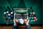 Man thumbs up playing online poker with laptop on a green table with chips all around, top view