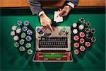 Online player's hands with laptop and stack of chips all around on green table top view, he is holding two ace cards