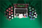 Poker and casino online gaming concept with laptop, cards and stacks of chips on green table, top view