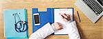 Doctor working at office desk writing medical records on a clipboard hands close up top view