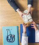 Male patient having a medical visit and bribing a greedy doctor with a lot of money, top view unrecognizable people