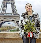 The Party Season in Paris. Portrait of happy trendy woman with Christmas tree in fur coat in the front of Eiffel tower in Paris, France
