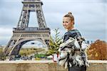 The Party Season in Paris. Portrait of smiling trendy fashion-monger with Christmas tree in fur coat in Paris, France