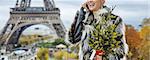 The Party Season in Paris. Portrait of happy modern fashion-monger with Christmas tree in fur coat in the front of Eiffel tower in Paris, France speaking on a smartphone