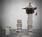 Businessman sitting on a pile of books with graduation cap