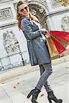 Stylish autumn in Paris. Full length portrait of happy trendy woman in trench coat with shopping bags in Paris, France